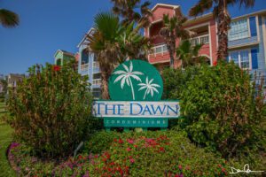 A sign of The Dawn Condominiums surrounded by plants